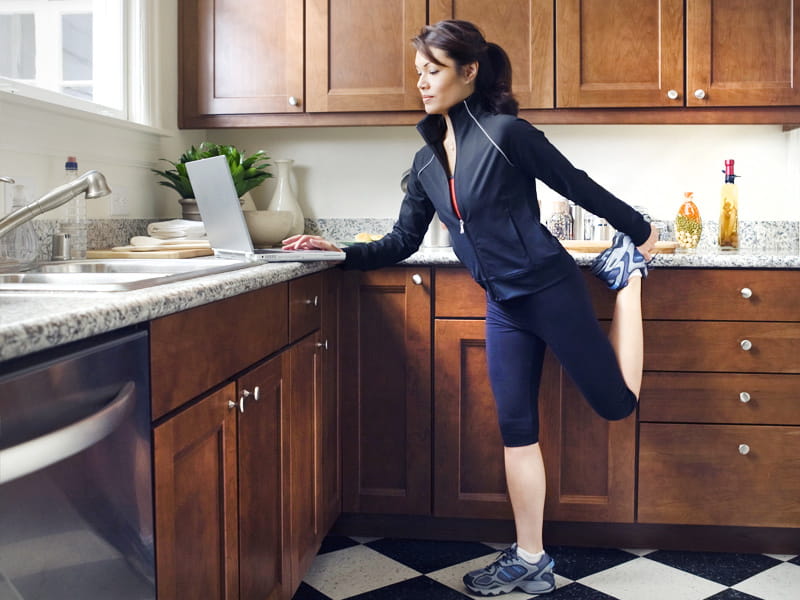 mujer ocupada trabaja en una computadora portátil en la cocina mientras hace ejercicio