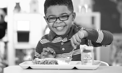 Elementary age black boy child smiling eating school lunch