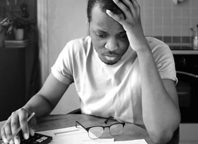 Black man at kitchen table, head in hands, looking at bills and paperwork