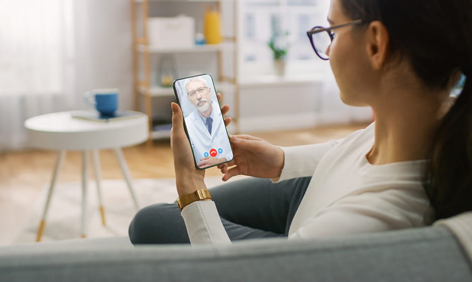 woman on couch participating in telehealth appointment with doctor on phone