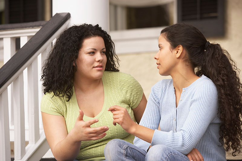 mujeres jóvenes conversando en escalones al aire libre