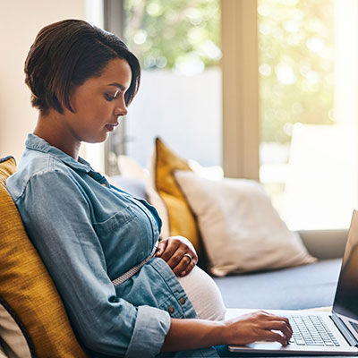 pregnant woman uses laptop on couch