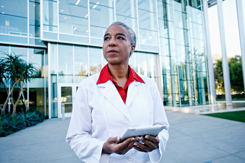 woman doctor or researcher holds tablet outside building GettyImages-738778729