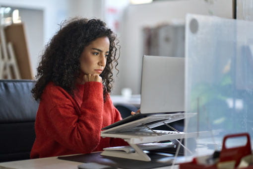 A young woman sitting at desk working on laptop analyzing data.