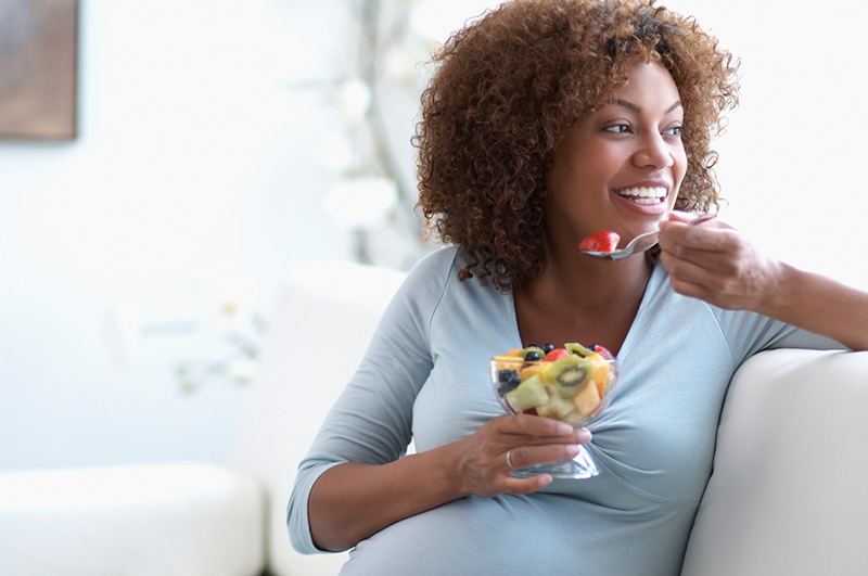 una mujer embarazada comiendo fruta en el sofá