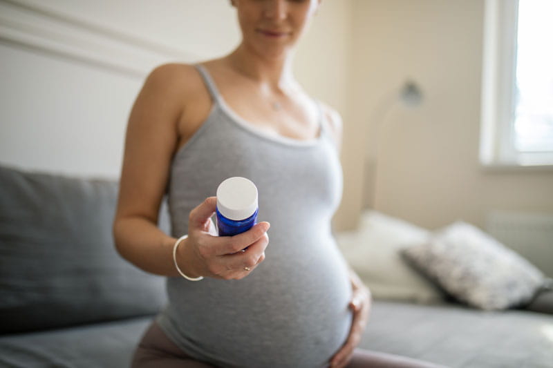 Mujer embarazada sosteniendo un frasco de píldoras.