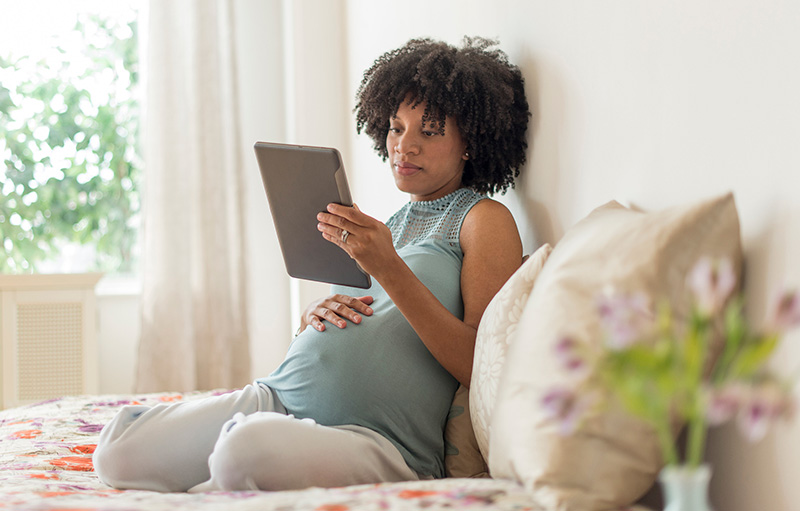 una mujer embarazada lee una tableta en la cama