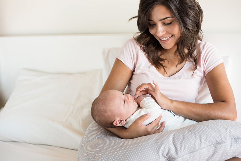 una madre joven sonriente que sostiene a su bebé en la cama