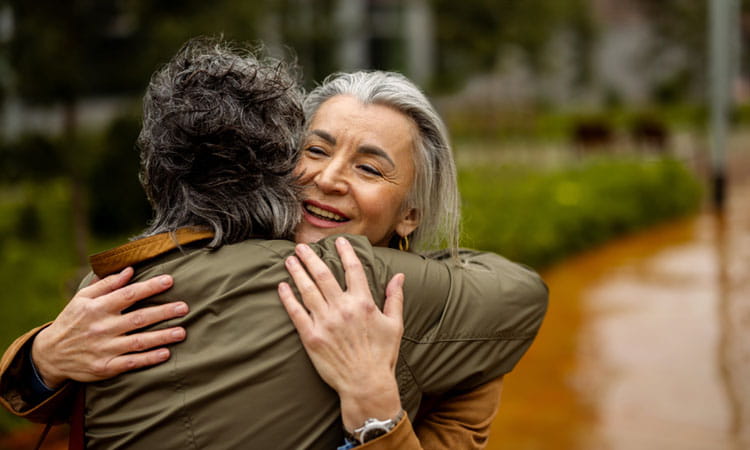 Two mature women hugging outside