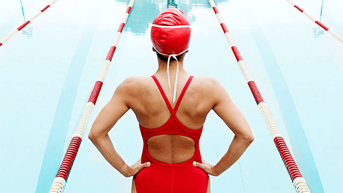 mujer en bañador de pie y de espaldas al borde de una piscina