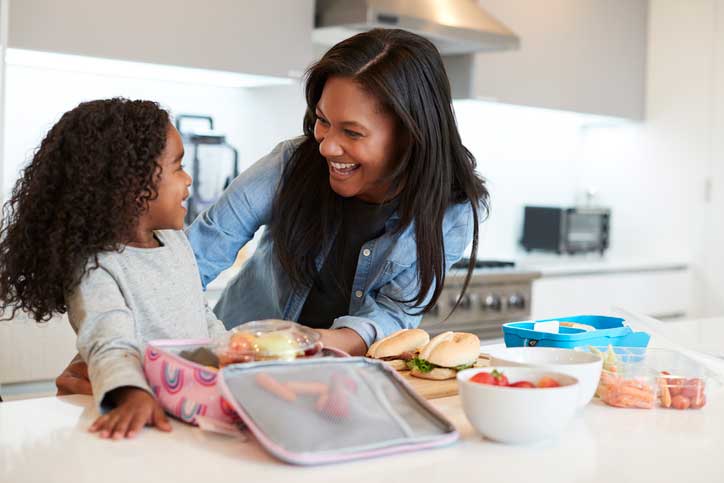 Hija en la cocina de una casa ayudando a la madre a preparar un almuerzo saludable en una lonchera