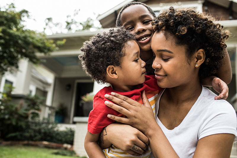 Mamá e hijos abrazándose al aire libre GettyImages-1182075825