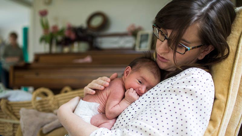 Mother cuddling newborn baby on comfy living room chair