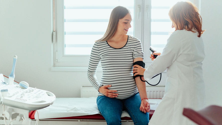Una ginecóloga que mide la presión arterial de su paciente embarazada que está sentada en la cama de un hospital