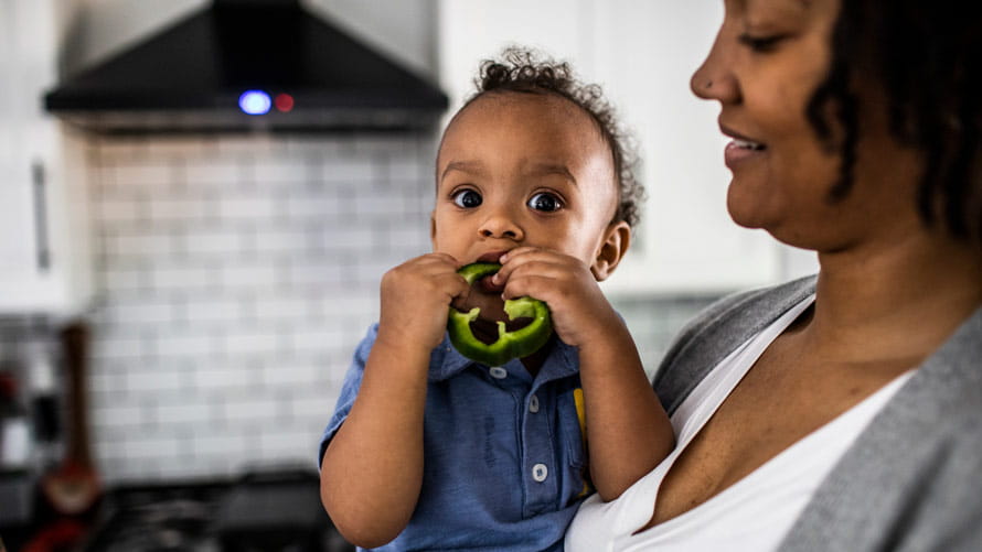 Una madre sostiene a su hijo pequeño que está comiendo un pimiento verde