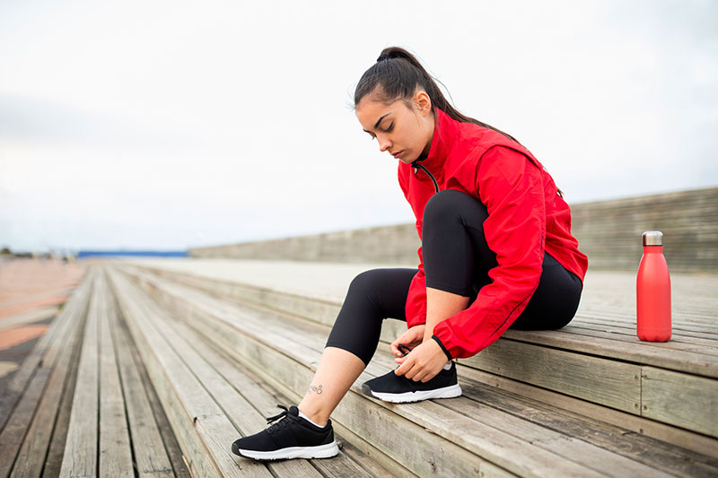 Young woman in red jacket ties shoe before outdoor workout