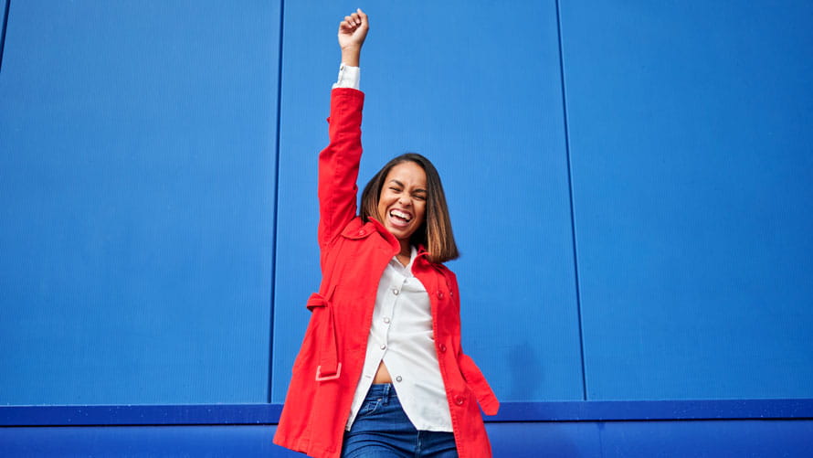 Happy woman with hand raised standing in front of blue wall