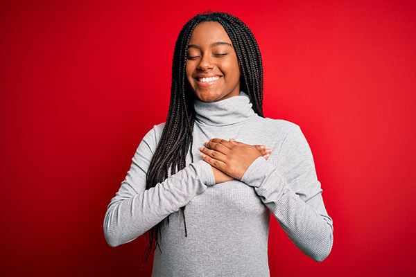 una joven feliz se toma las manos sobre el corazón una joven feliz se toma las manos sobre el corazón
