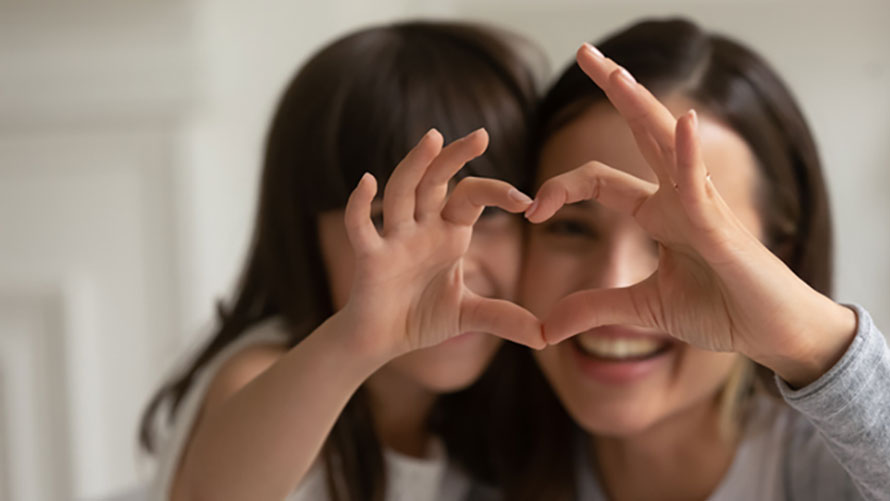 Happy young mother with little daughter making focused heart sign.