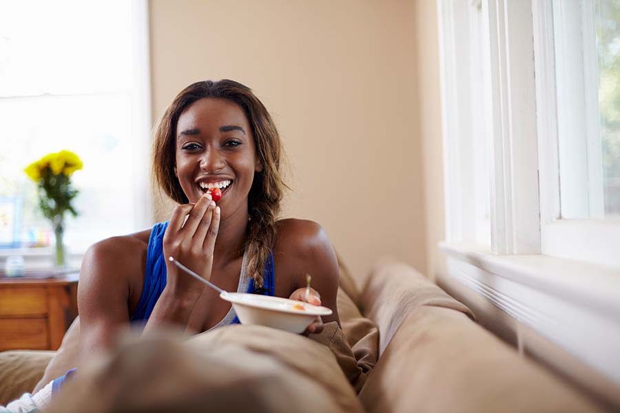 Mujer joven sentada en el sofá, comiendo y sonriendo