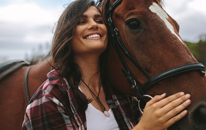 mujer sonriente abraza a caballo