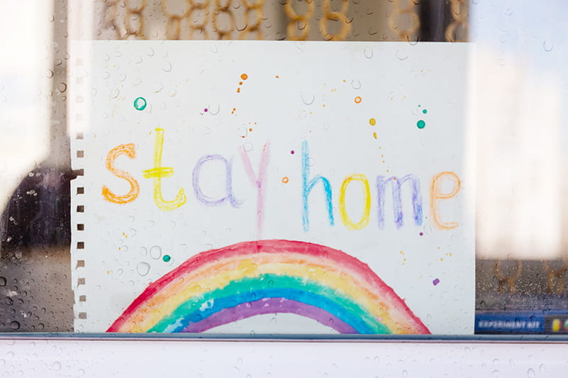 arcoíris de crayón con mensaje "quédese en casa" escrito en inglés en la ventana