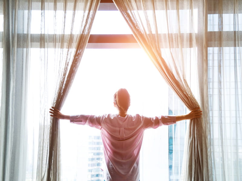 una mujer abre las cortinas al amanecer