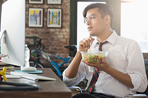 Un joven comiendo ensalada en un escritorio