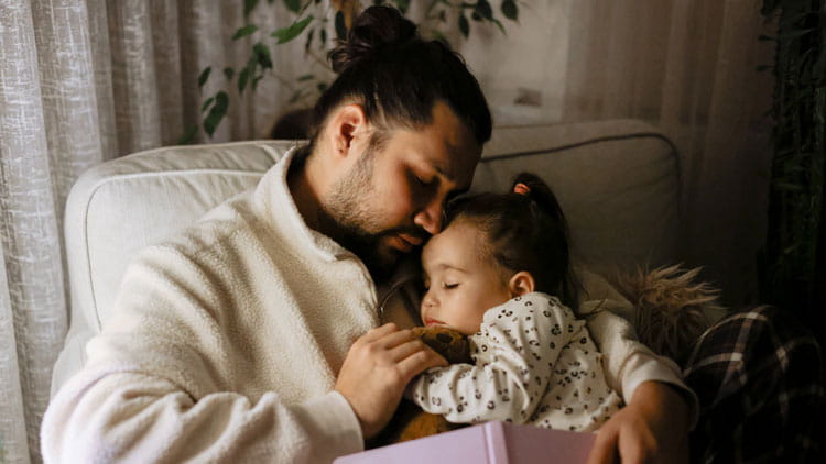 Father and daughter sleeping in a chair after reading a book.
