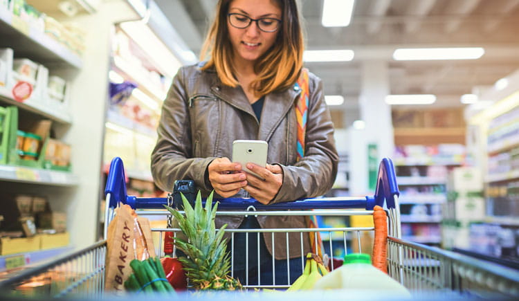 Young women grocery shopping uses her smartphone to view her grocery list. 