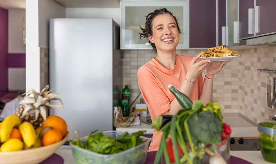 happy young woman holding plate of food in her kitchen