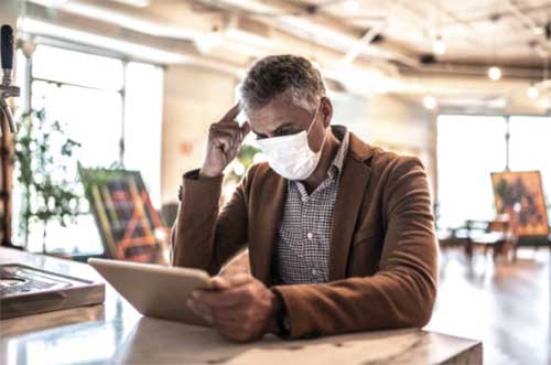 man wearing face mask while reading tablet