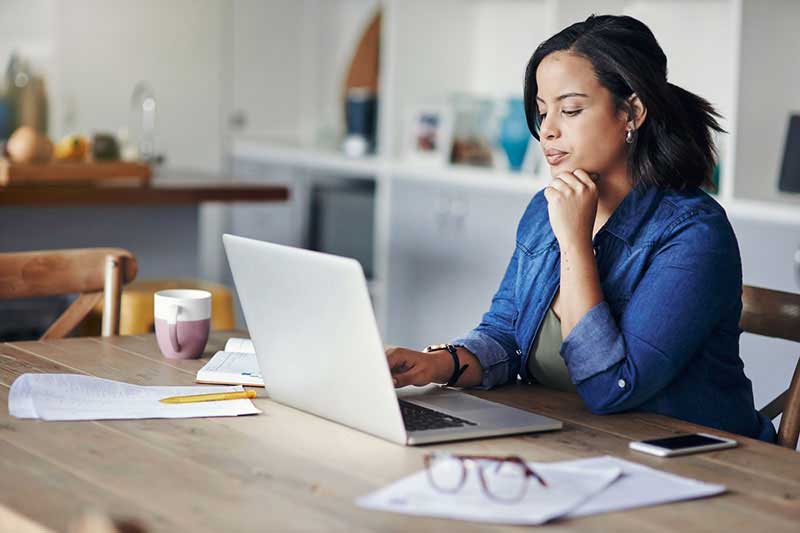 mujer sentada frente una mesa mirando una computadora portátil