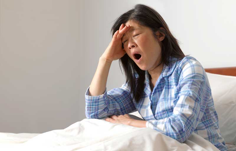 una mujer somnolienta bostezando en su cama