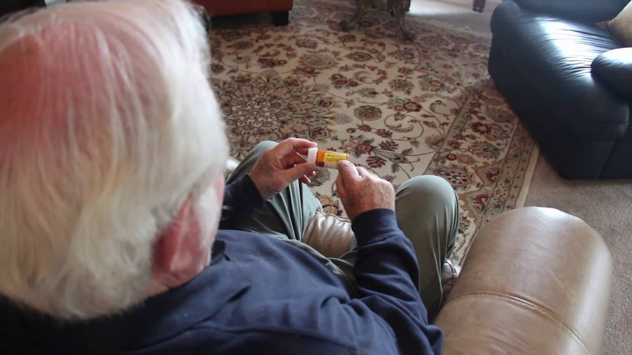 Hombre sentado en una silla sacando medicamentos de un frasco