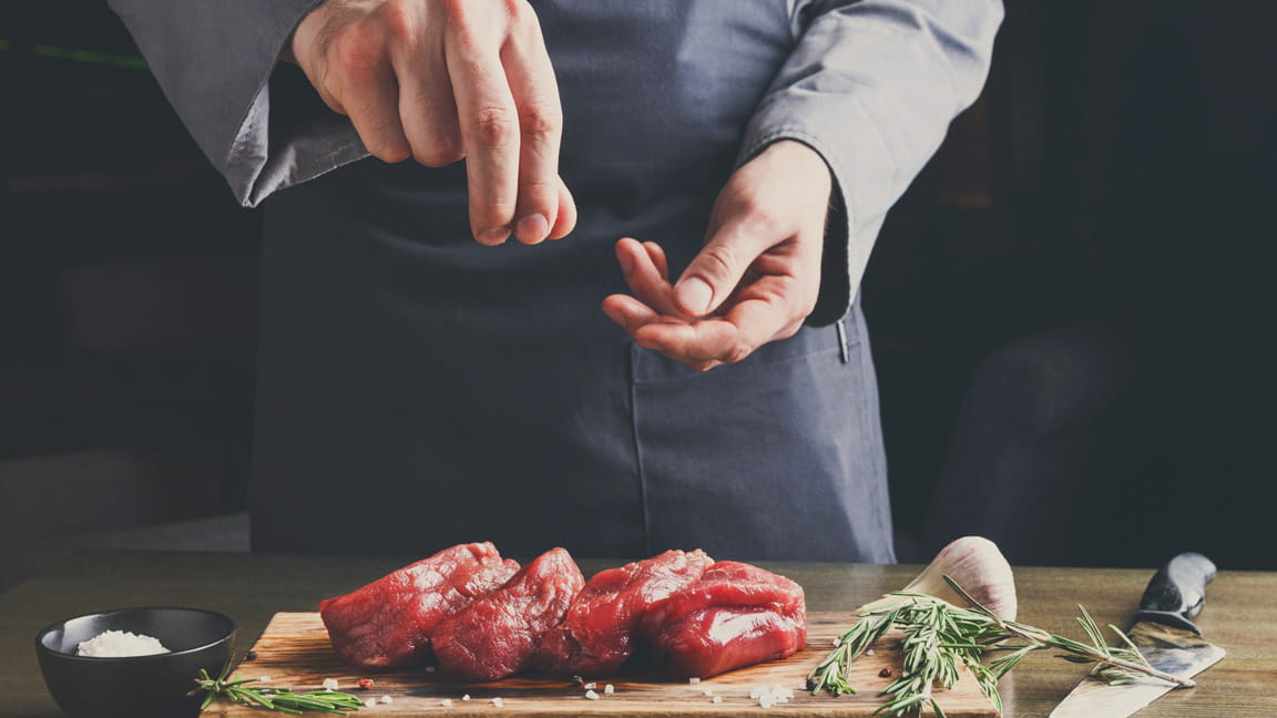 manos de hombre añadiendo sal a la carne mientras cocina