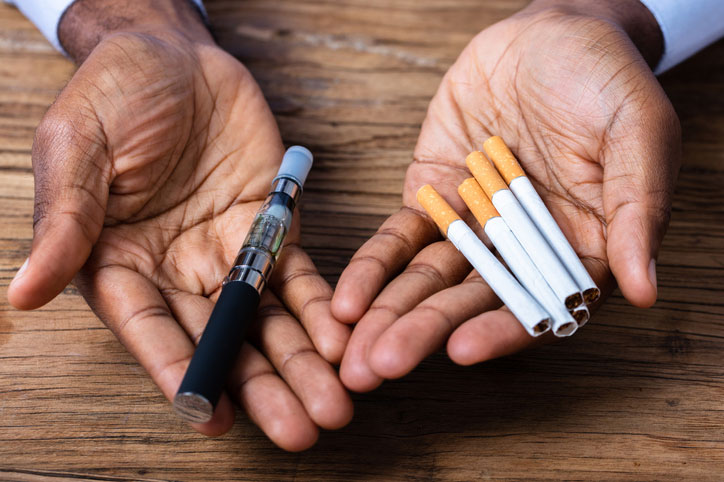 hombre sujetando un vapeador tipo lápiz y cigarrillos