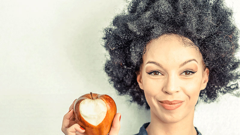 mujer de pelo gris comiendo una manzana mordida en forma de corazón