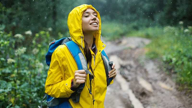 Mujer joven con chubasquero disfruta de la naturaleza bajo la lluvia
