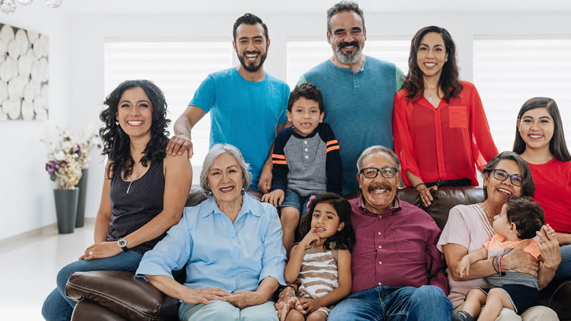 Familia hispana multigeneracional sentada alrededor de un sofá y posando para la cámara