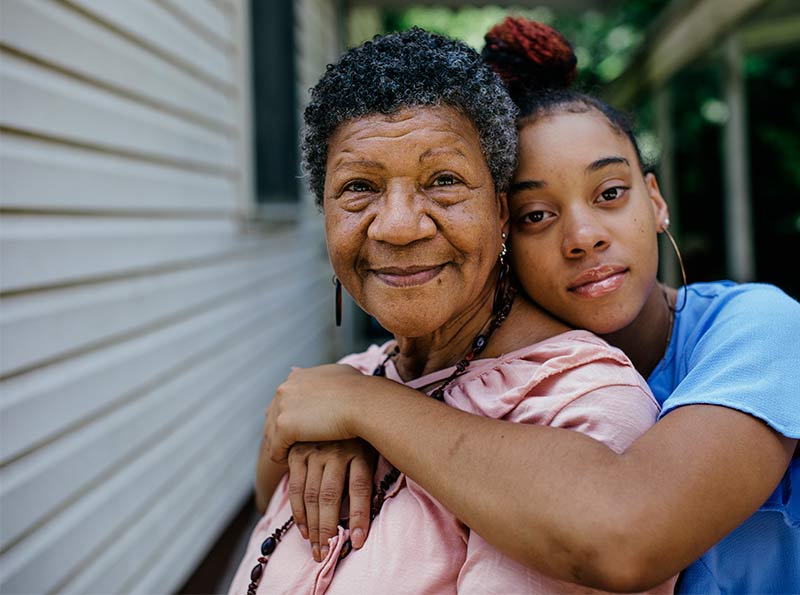 A teenaged Black girl with her arms wrapped around her smiling grandmother