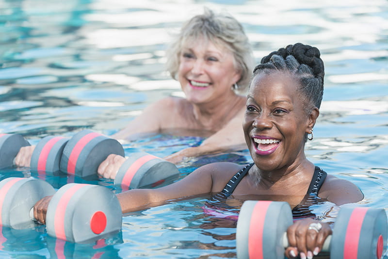 una mujer de raza negra de edad avanzada y su amiga hacen ejercicios aeróbicos acuáticos