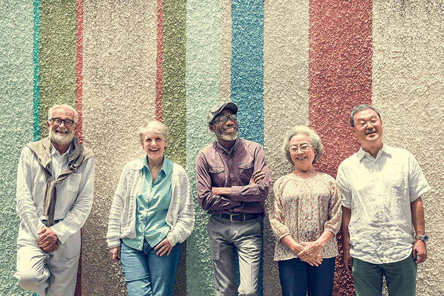 A diverse group of older people standing and smiling against a colorful striped wall.