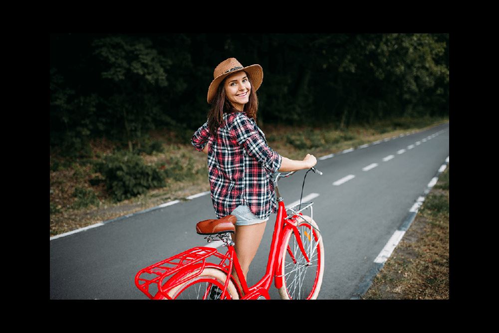 young woman walking red vintage bicycle down a tree-lined street