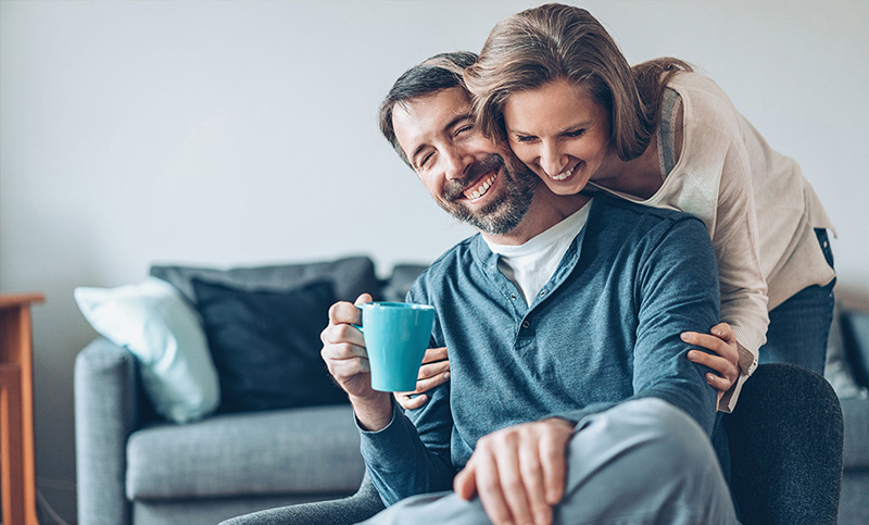 Woman hugs man from behind who is drinking coffee Woman hugs man from behind who is drinking coffee