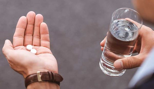 primer plano de manos masculinas con unas píldoras y un vaso de agua