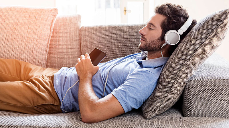 Man laying on couch listening with headphones Man laying on couch listening with headphones
