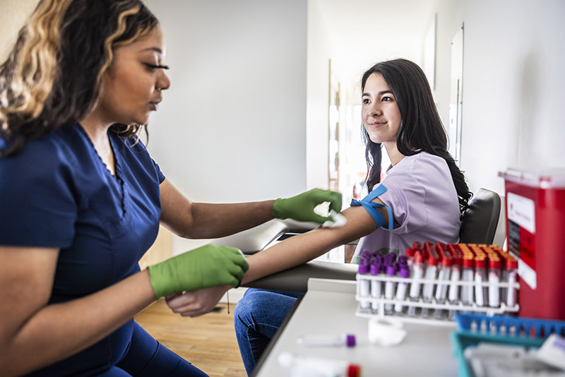 Female nurse drawing blood sample from teenage girl in medical office
