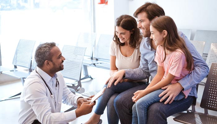 Smiling doctor talking with girl's father and mother