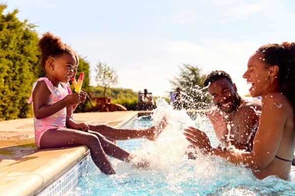 Young kids sitting on the side of a swimming pool splashing parents